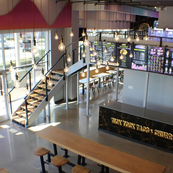 Interior of Tick Tock Taco & Churros with a long bar, dining tables, and a staircase.