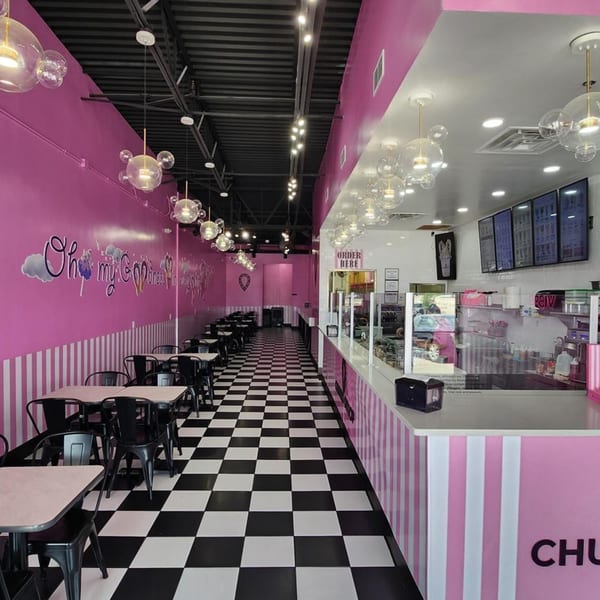 A vibrant pink and white dessert shop interior with a checkered floor and bubble-shaped light fixtures.